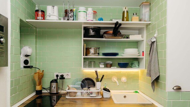 A kitchen with green tiles, a wooden countertop, a stove, a sink, and various kitchen utensils and appliances. - Malvasia Harbor's Light (La Vila Joiosa)
