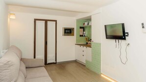A compact living space with a sofa, a kitchenette, a television, and a door. - Malvasia Harbor's Light (La Vila Joiosa)