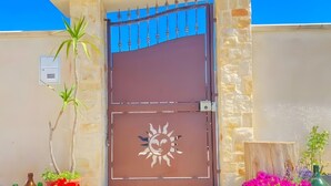 A gated entrance with a decorative sun motif, a stone wall, and potted plants. - Villa 'Regina' with Private Garden and Air Conditioning (Taranto)