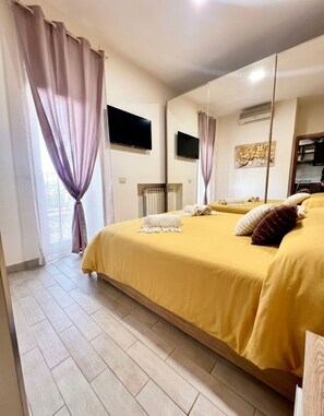 A bedroom with a large bed, a flat-screen TV, a radiator, and a window with curtains. - Fiorucci Apartments - Veronica's House (Roma)