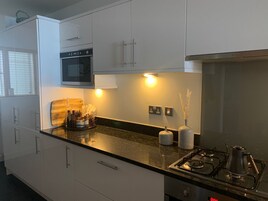 Una cocina moderna con gabinetes blancos, horno empotrado, estufa a gas y una encimera con utensilios básicos de cocina.