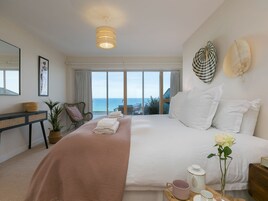 Un dormitorio con una cama grande, una mesita de noche, una silla, una planta en maceta y vistas al mar.