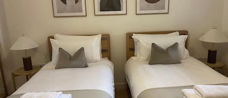 Une chambre d’hôtel avec deux lits, chacun équipé d’un oreiller et d’une table de chevet avec une lampe, et une œuvre d’art abstraque encadrée au-dessus des lits.