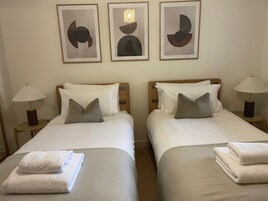 Habitación de hotel con dos camas, cada una con un almohadón, una mesita de noche con lámpara y una obra de arte abstracta enmarcada sobre las camas.
