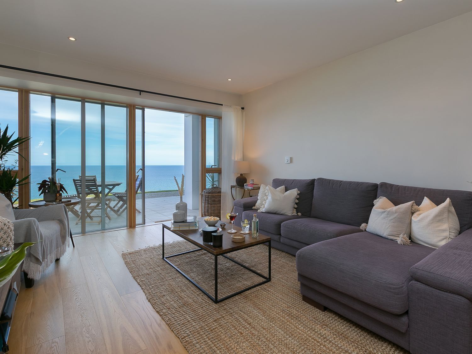Un salón amplio con un sofá grande, una mesa de centro y vistas al mar a través de ventanales de gran altura.