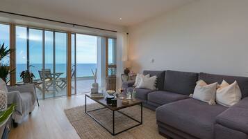 Un salón amplio con un sofá grande, una mesa de centro y vistas al mar a través de ventanales de gran altura.