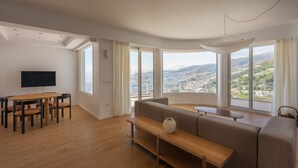 Ein geräumiges Wohnzimmer mit großem Fenster, Essbereich und Flachbildfernseher.