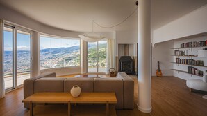 Ein modernes Wohnzimmer mit großem Fenster, Kamin, Bücherregal und einer Gitarre.
