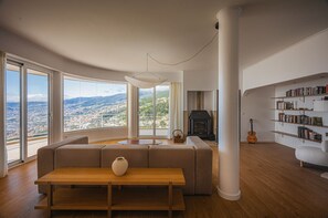 Ein modernes Wohnzimmer mit großem Fenster, Kamin, Bücherregal und einer Gitarre.