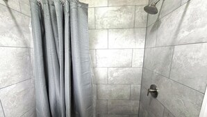 A shower with a metal showerhead, a tiled wall, and a shower curtain. - Friendship Inn Near Golf Course Ocala Fl (Ocala)