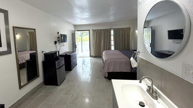 A hotel room with a bed, a desk, a dresser, a large mirror, a TV, and a bathroom with a sink and mirror. - Friendship Inn Near Golf Course Ocala Fl (Ocala)