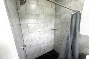 A shower with grey tiles, a showerhead, a glass door, and a curtain. - Friendship Inn Near Golf Course Ocala Fl (Ocala)