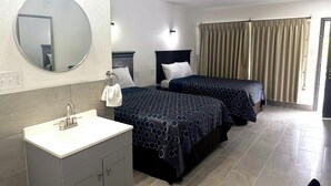 A hotel room with a round mirror, two beds with patterned bedspreads, a white sink, and a window with curtains. - Friendship Inn Near Golf Course Ocala Fl (Ocala)