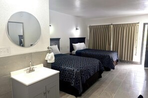 A hotel room with a round mirror, two beds with patterned bedspreads, a white sink, and a window with curtains. - Friendship Inn Near Golf Course Ocala Fl (Ocala)