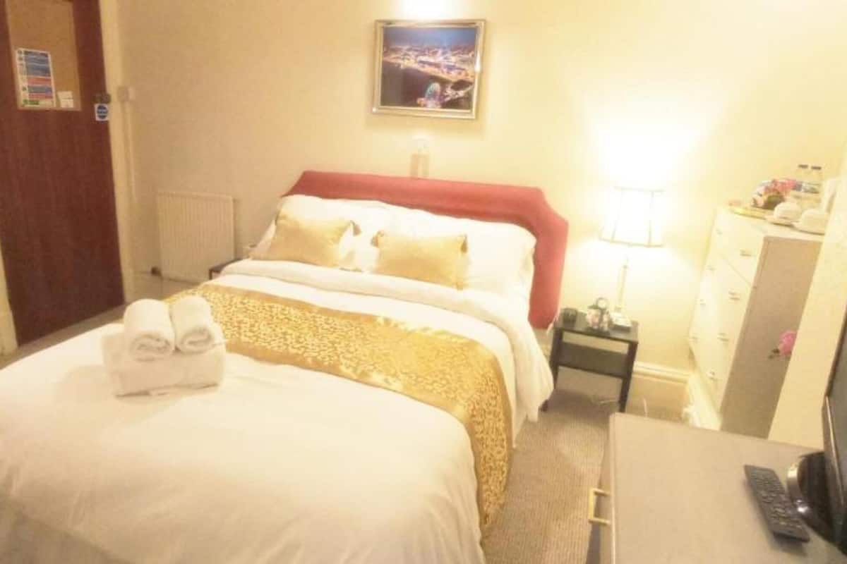 A hotel room with a bed, a desk with a computer, a chair, a nightstand, and a wall-mounted TV.
