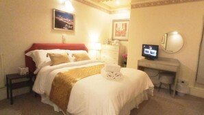 Una habitación de hotel con cama, escritorio, televisor y mesita de noche.