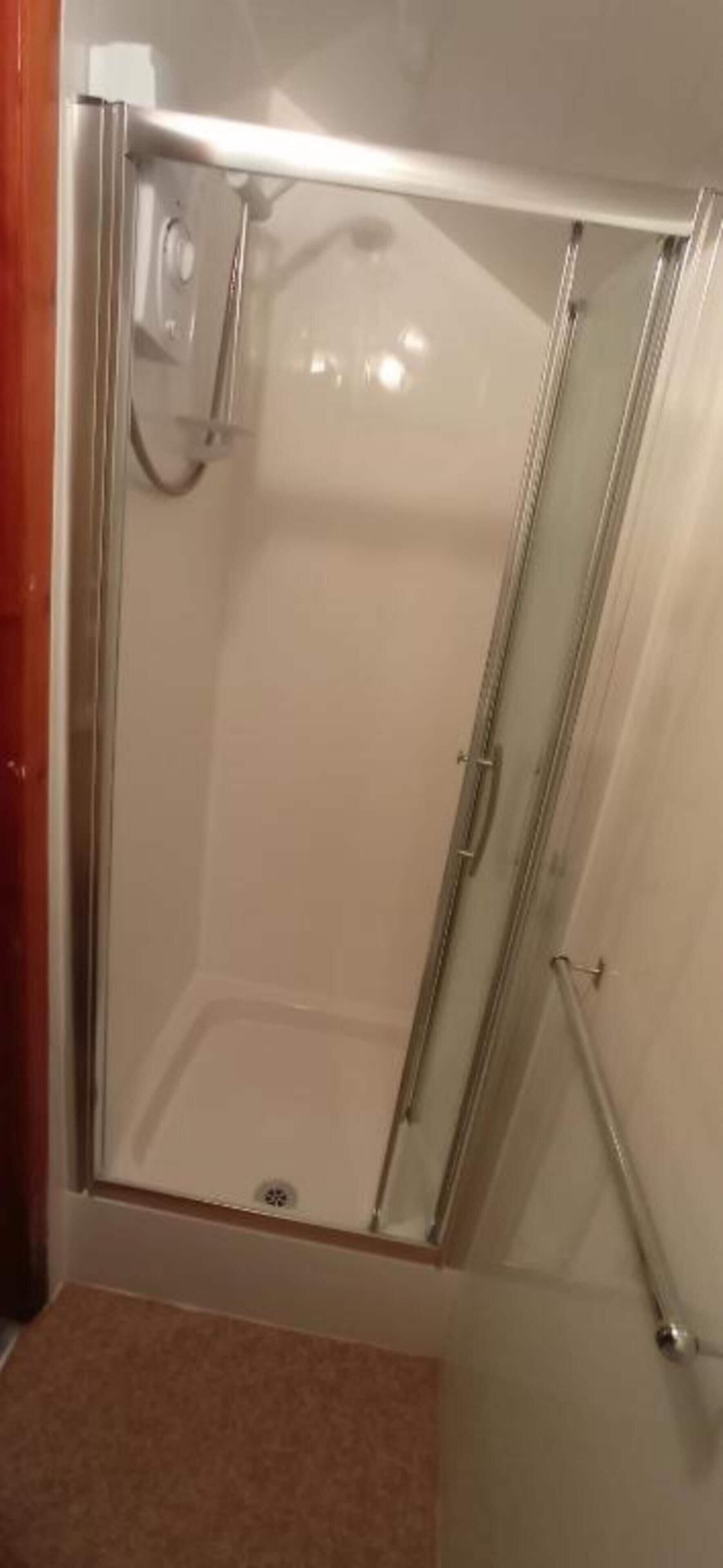 A glass-enclosed shower stall with a showerhead and a control panel.