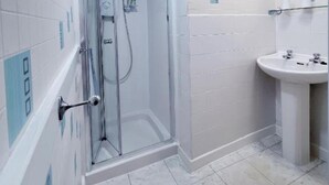Un baño con cabina de ducha de vidrio, un lavamanos y paredes con azulejos.