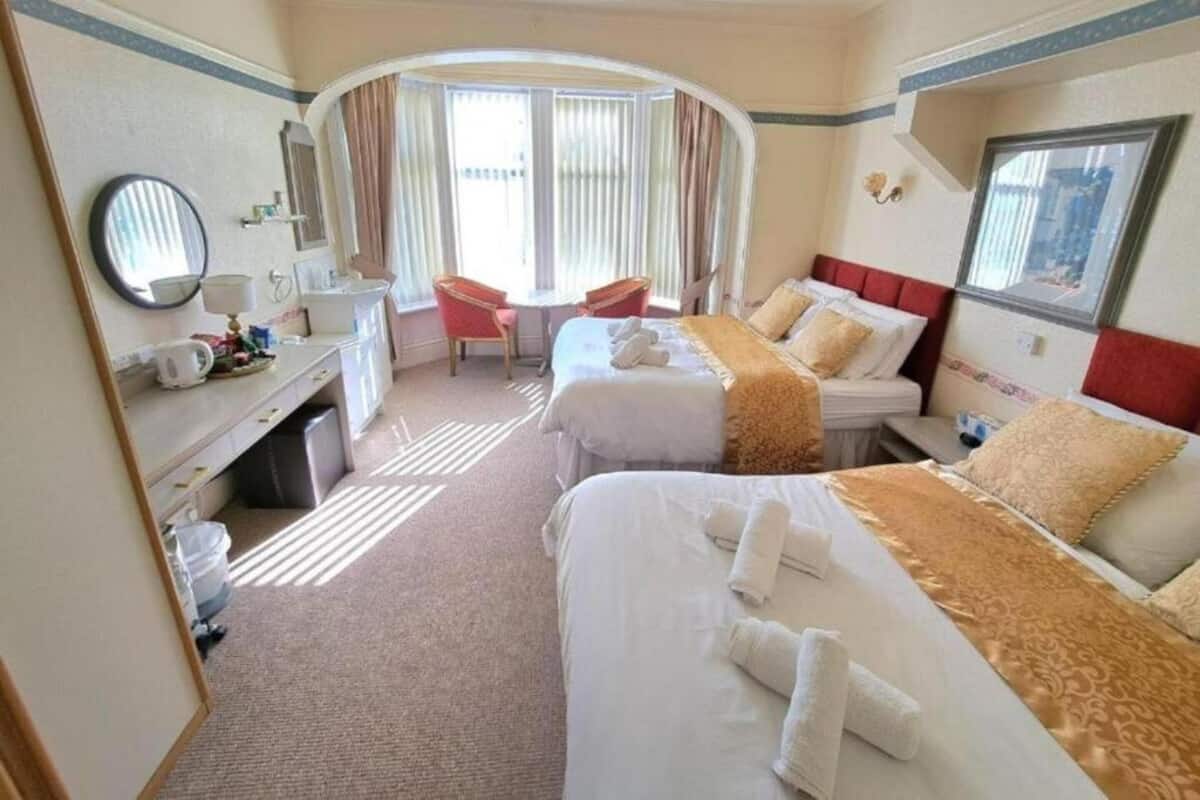 A hotel room with two beds, a desk, a chair, a window with curtains, and a mirror.