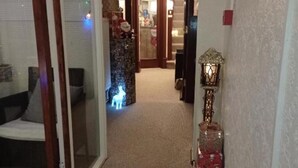 Un pasillo con piso alfombrado, una puerta de vidrio a la izquierda y un aplique en la pared a la derecha.