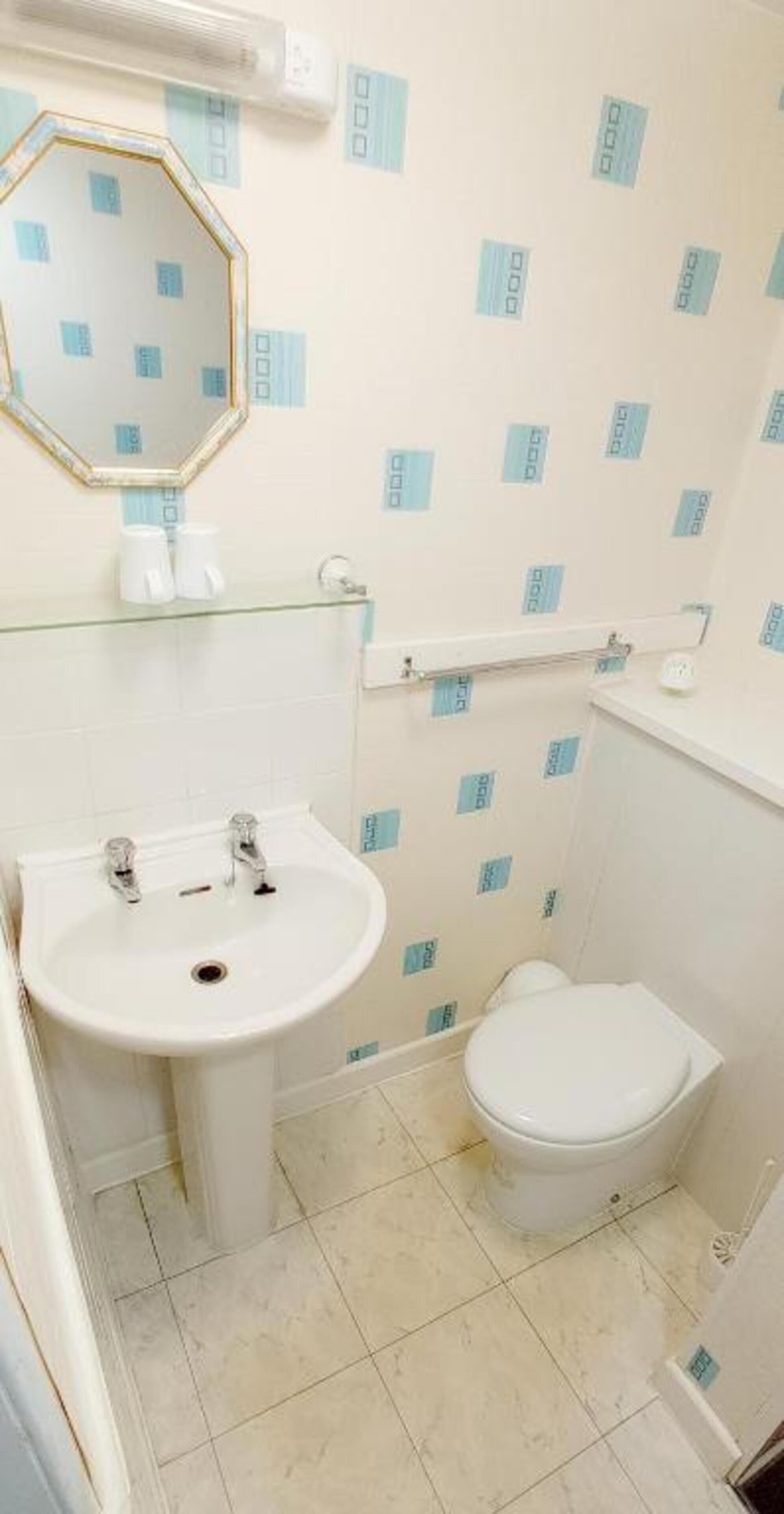 A bathroom with a white sink, a mirror, a toilet, and patterned wallpaper.