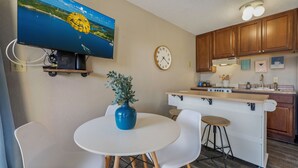 A compact kitchen with a dining area, a clock, and a television displaying a scenic view. - Cozy Lake Escape - King Bed • Private Deck (Osage Beach)