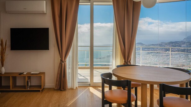 A modern living room with a large window, a round wooden table, and a flat-screen TV. - 2 Bedroom | 180° View + Balcony | Bathtub (Funchal)