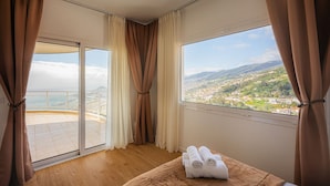 A room with a large window, a bed with a brown headboard, and a pair of towels on the bed. - 2 Bedroom | 180° View + Balcony | Bathtub (Funchal)
