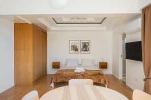 A bedroom with a bed, two bedside tables, a TV, a ceiling light, and a window. - Panoramic Ocean View | Pool & Garden | 2 Bedrooms (Funchal)