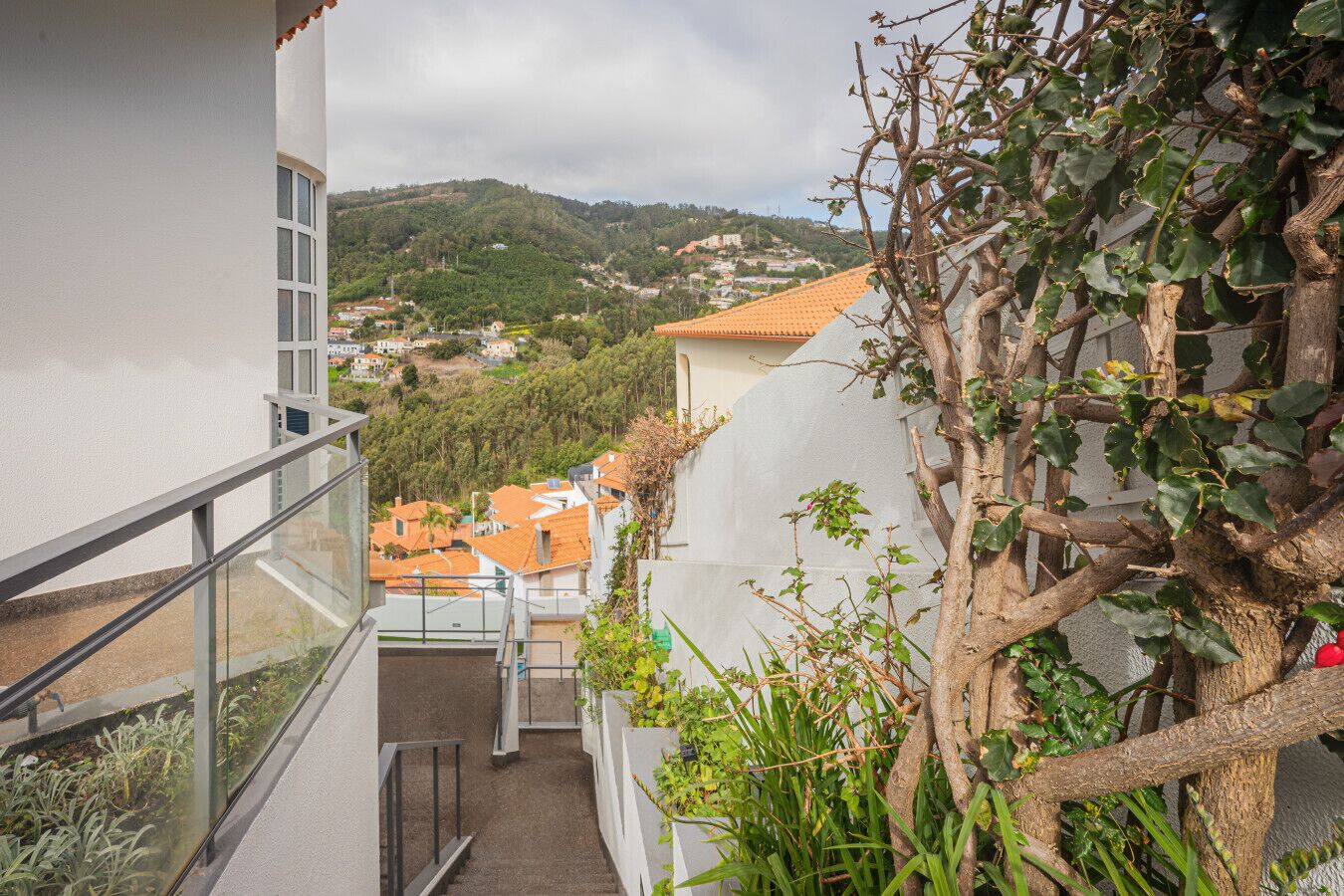 A residential area with a staircase leading to a balcony overlooking a hillside with houses.