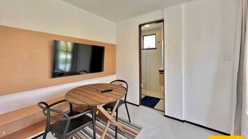 A modern room with a flat-screen TV mounted on a wooden panel, a round wooden table with chairs, and a door leading to a bathroom.