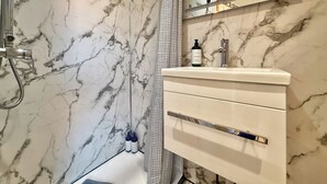 A bathroom with a marble wall, a shower, a sink with a bottle of lotion, and a mirror. - Modern compact Studio APT near City Centre (Essex)