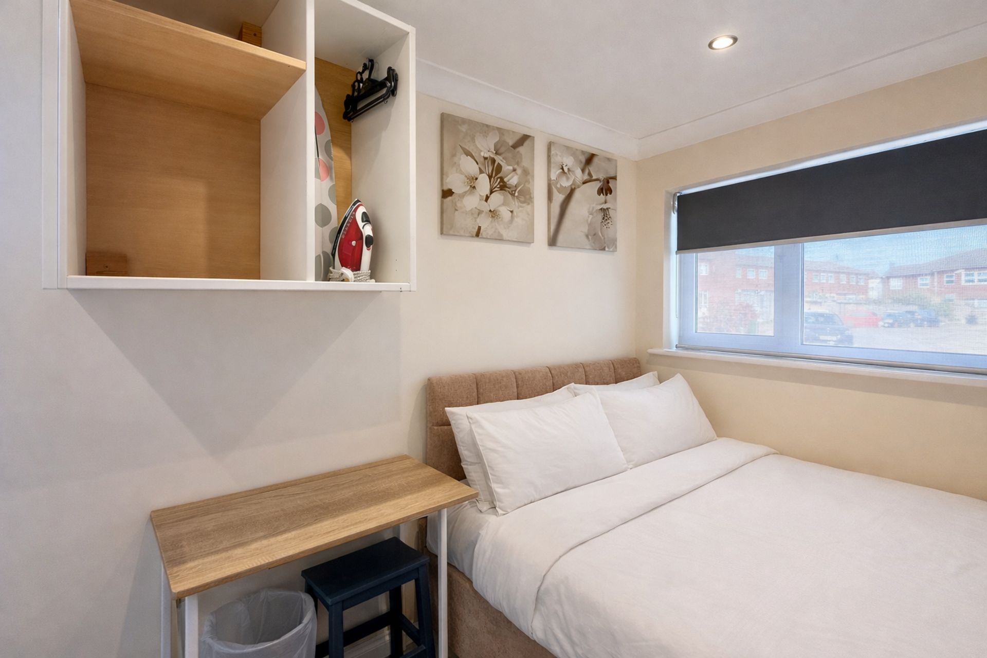 A bedroom with a bed, a desk, a chair, a window, and artwork on the wall.