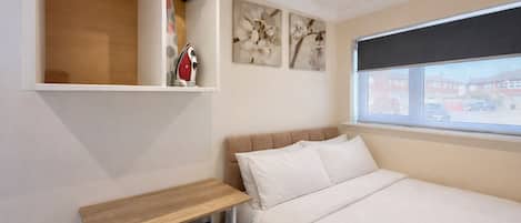 A bedroom with a bed, a desk, a chair, a window, and artwork on the wall.