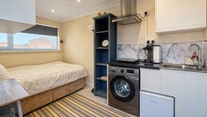 A compact hotel room with a bed, a washing machine, a small kitchenette, and a window. - Modern compact Studio APT near City Centre (Essex)