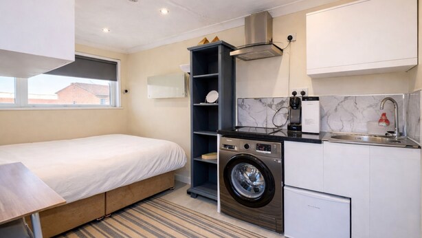 A compact hotel room with a bed, a washing machine, a sink, and a small kitchenette. - Modern compact Studio APT near City Centre (Essex)