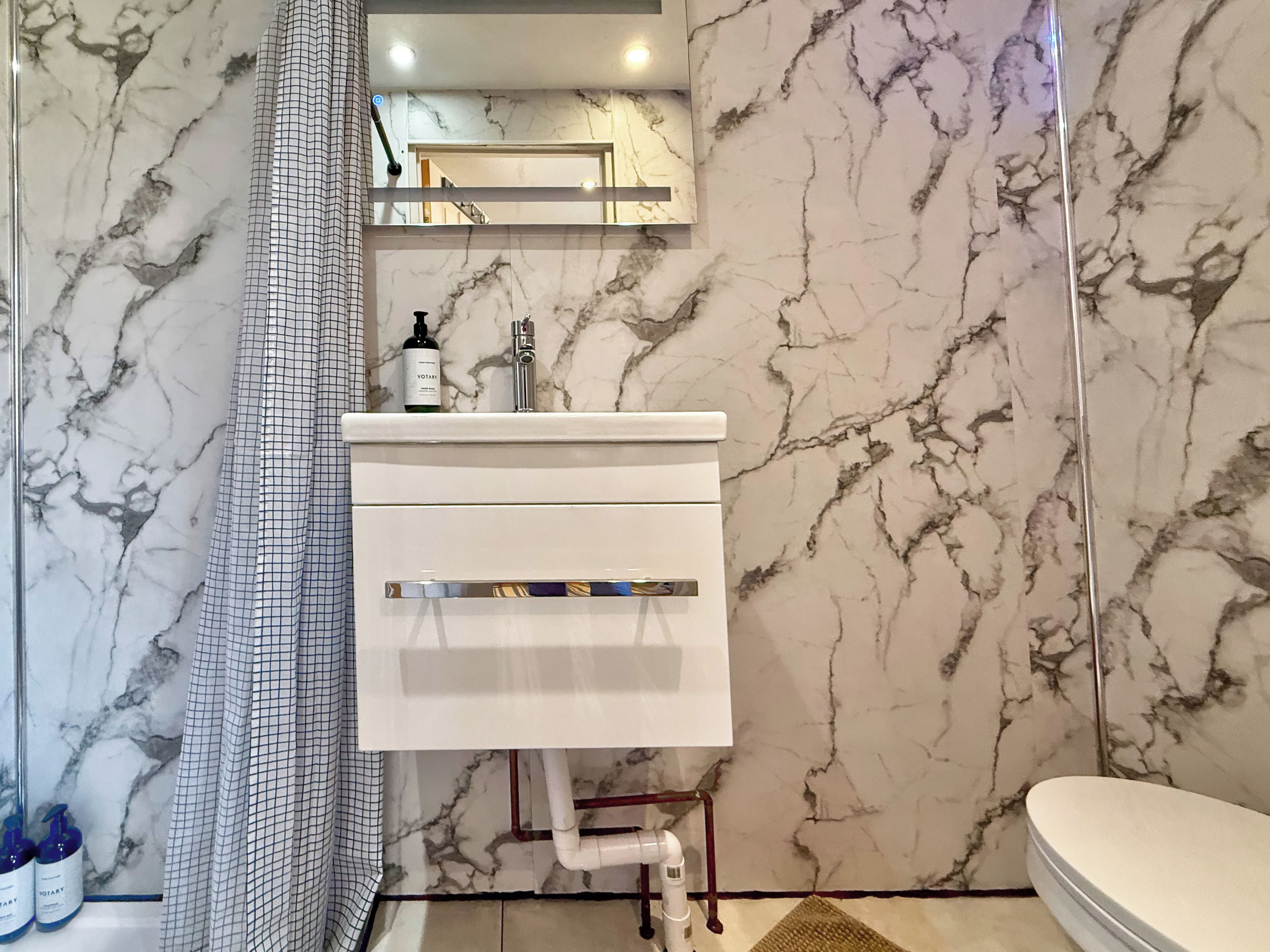 A bathroom with a marble wall, a white sink, a shower curtain, and toiletries.