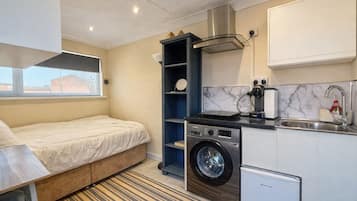 A compact hotel room with a bed, a washing machine, a small kitchenette, and a window.