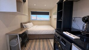 A compact hotel room with a bed, a washing machine, a small desk, and a window with a view. - Modern compact Studio APT near City Centre (Essex)