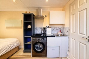 A compact hotel room with a bed, a washing machine, a compact refrigerator, a coffee maker, and a small sink. - Modern compact Studio APT near City Centre (Essex)