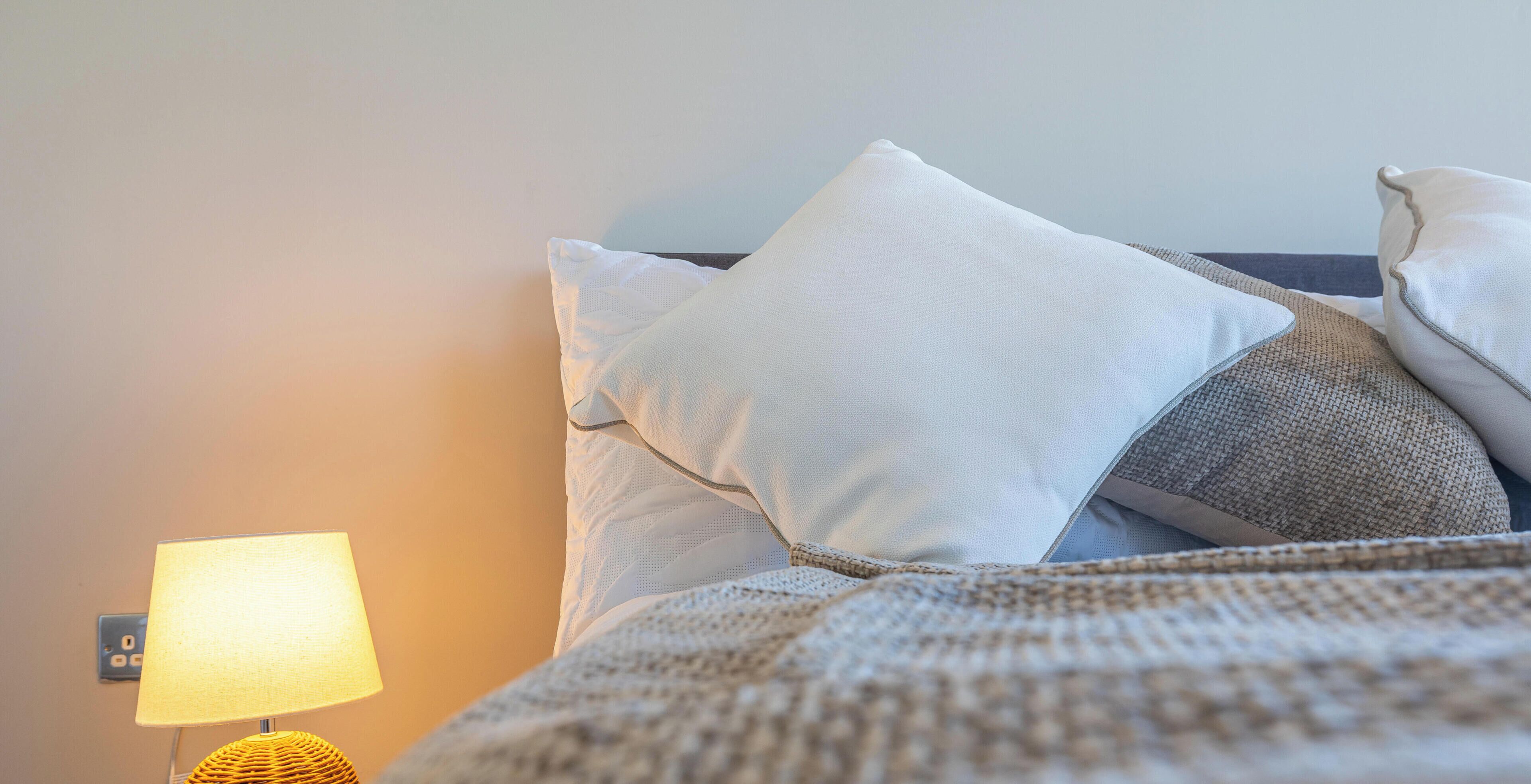 A bed with pillows and a lamp on a nightstand.