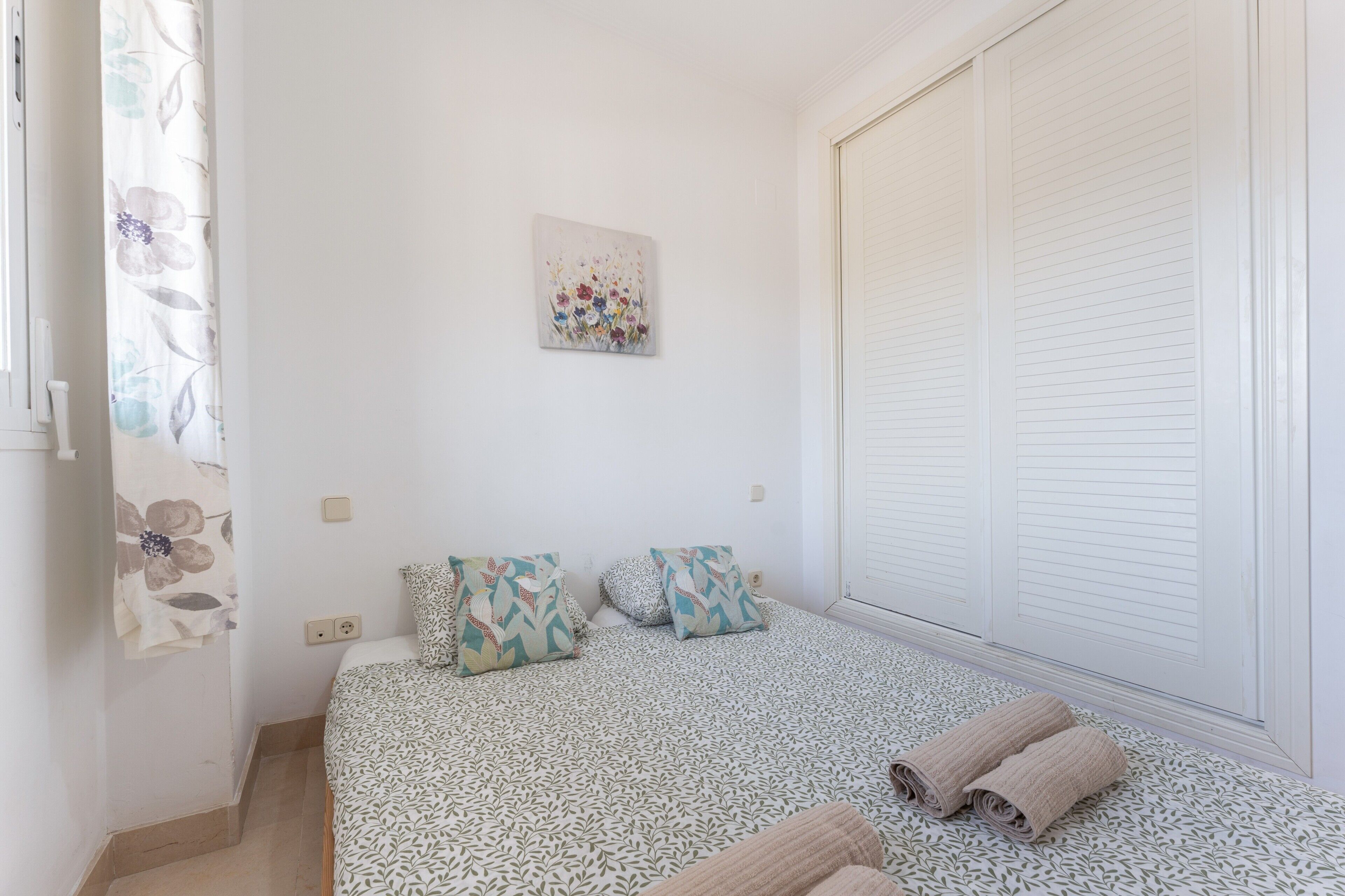 A bedroom with a bed, two pillows, a wall-mounted artwork, a window with blinds, and a door.