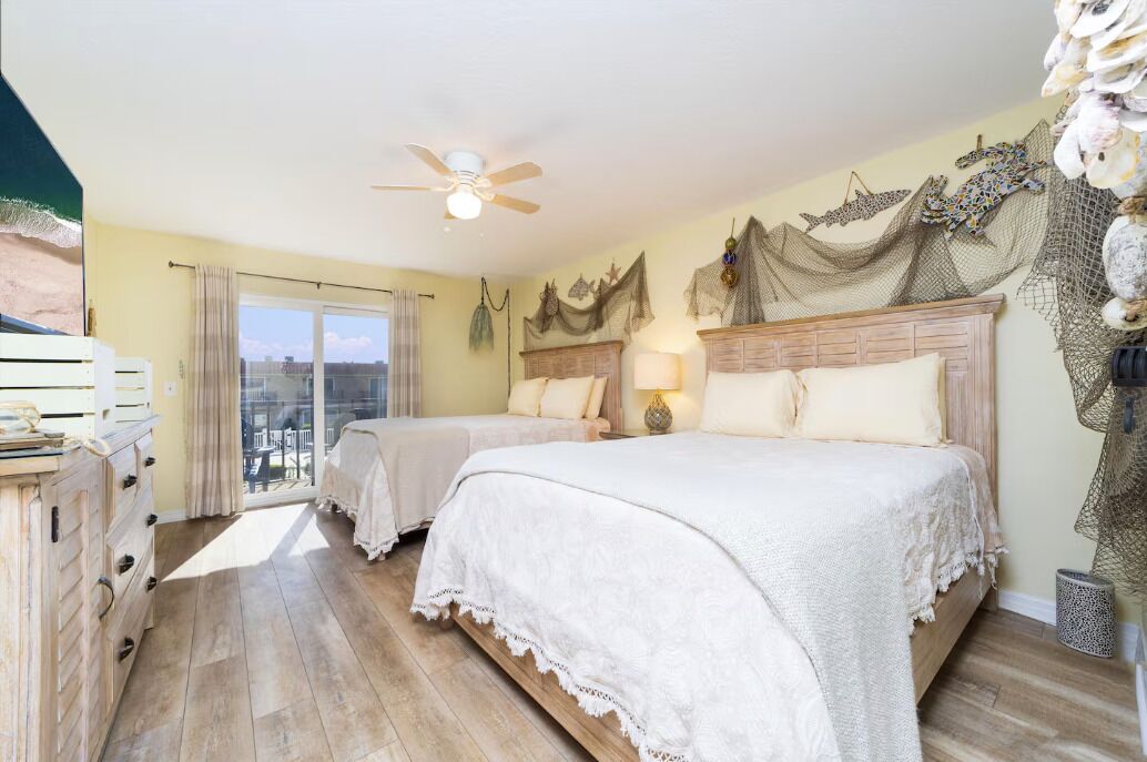 Une chambre d’hôtel avec deux lits, un ventilateur de plafond, un balcon avec vue et un mur décoratif.