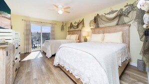 Camera d'albergo con due letti, una ventola a soffitto, un balcone con vista e una parete decorativa.