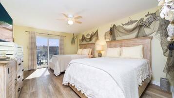Une chambre d’hôtel avec deux lits, un ventilateur de plafond, un balcon avec vue et un mur décoratif.