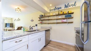 Cucina con mobili bianchi, un piano di lavoro in granito, un frigorifero in acciaio inossidabile e mensole in legno sopra il bancone.