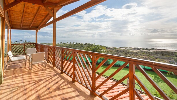 A wooden deck with chairs, a view of the sea, and a green landscape. - Villa Horizonte with Sea Views, Wi-Fi and Air Conditioning (Tijoco Bajo)