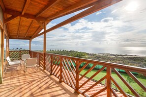 Une terrasse en bois avec des chaises, une vue sur la mer et un paysage verdoyant.