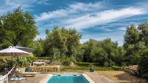 Um deck de madeira com piscina, cadeiras de descanso e uma rede.