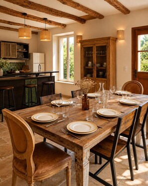 A dining table set with plates, glasses, and cutlery, wooden chairs, a vase with dried flowers, and a kitchen area with a refrigerator and cabinets. - Bastide de 1855 au pied du Garlaban | Terrace, pool & Provencal charm (Aubagne)